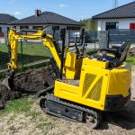 Mini excavator digging a hole in the garden along the fence to the drainage pipes.