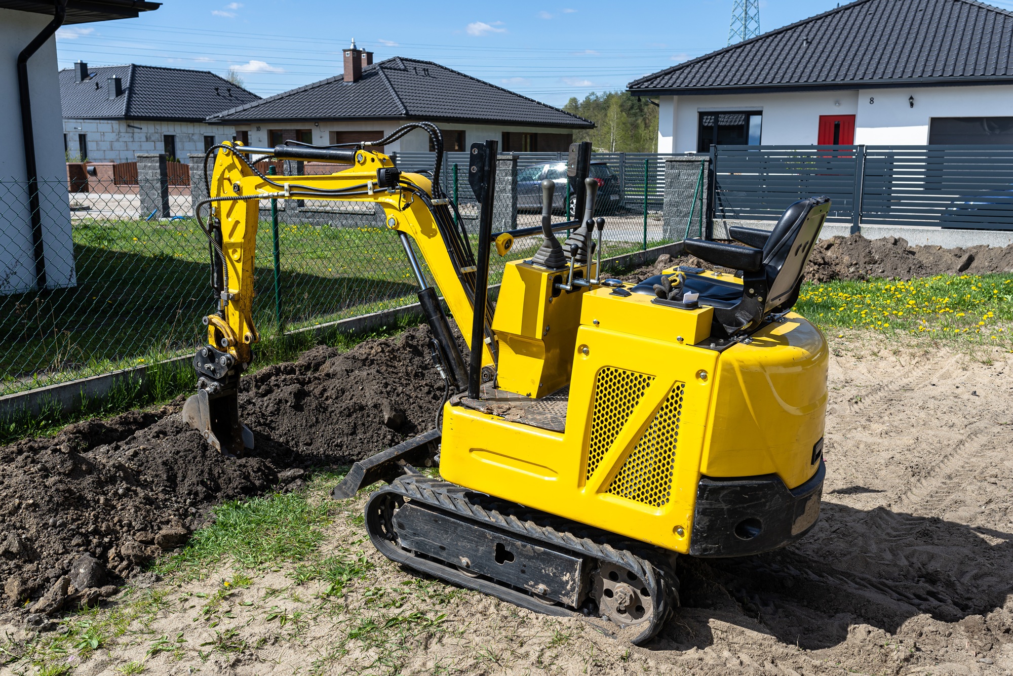 Mini excavator digging a hole in the garden along the fence to the drainage pipes.